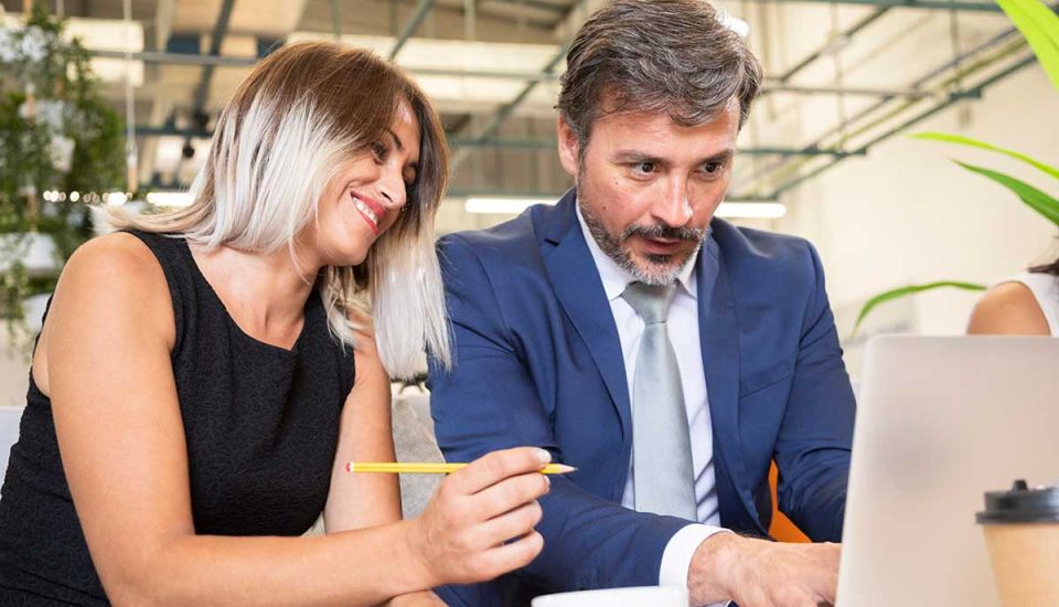 A man and woman are seated together, intently examining the screen of a laptop in a collaborative setting.