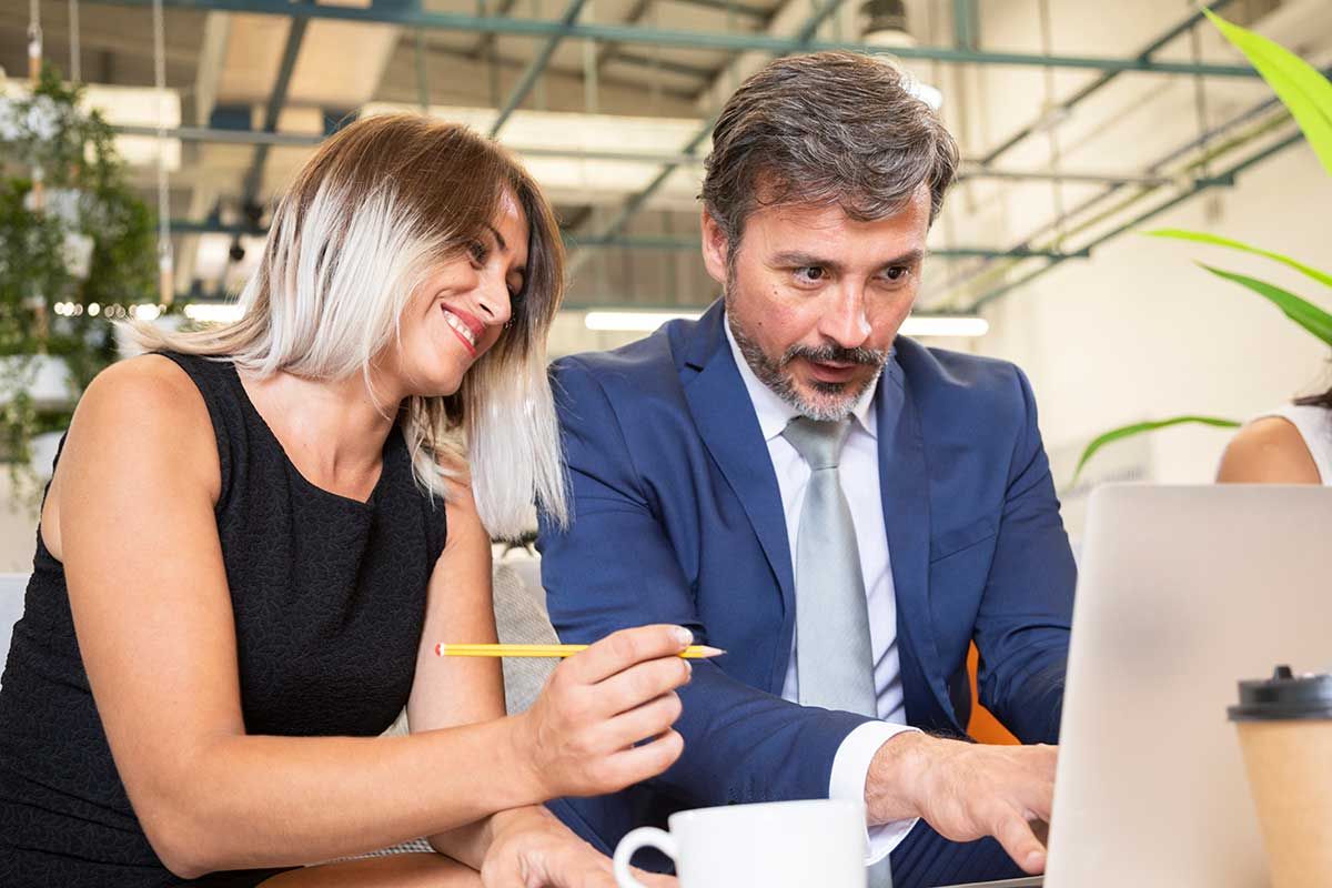 A man and woman are seated together, intently examining the screen of a laptop in a collaborative setting.