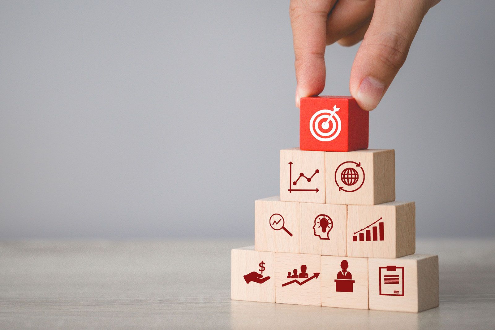 Hand arranging wood blocks stacked with an arrow icon of a target