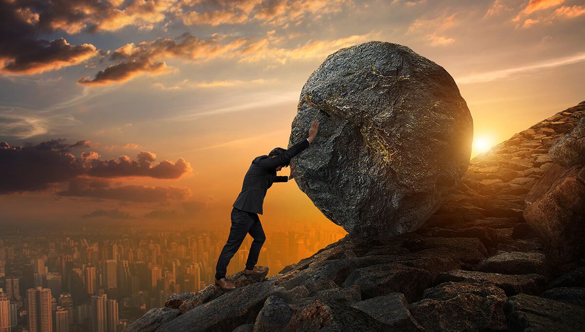 A business man pushing a large stone up hill